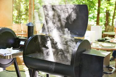 the lid of a pellet grill open and it releasing smoke 