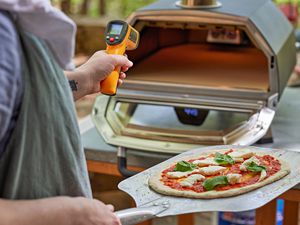 A person checking the temperature of the Ooni Karu 16 with an infrared thermometer