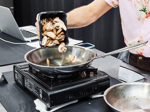 a person pouring mushroom into a stainless steel skillet