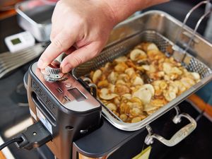 A person turning the control knob of a deep fryer